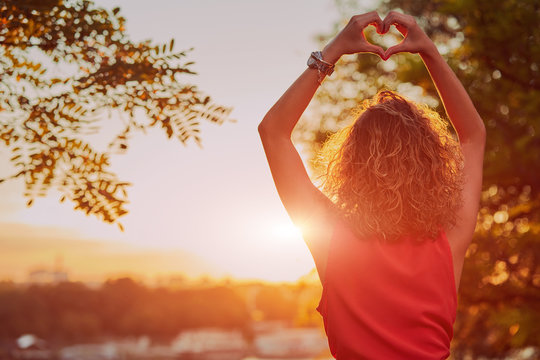 Woman holding heart shape and enjoying the sunset/sunrise.