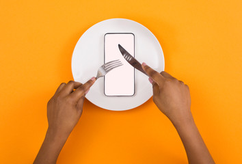 Woman eating blank smartphone with knife and fork