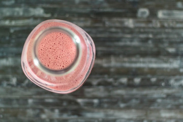 Top view of bottle with strawberry milkshake on wooden table
