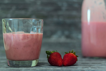 Glass with strawberry milkshake, strawberries and bottle on the background