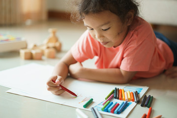 Cute little asian girl drawing homework and writing with color Wax crayons on paper in her home - Powered by Adobe