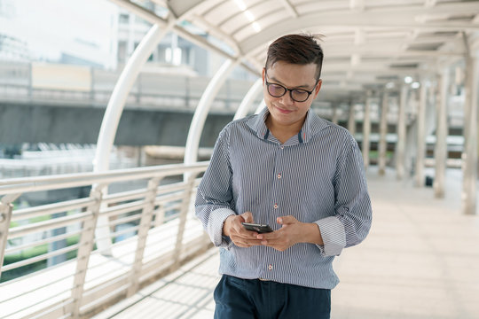 Portrait of asian young businessman standing at Outside Office. Young businessman wear suit smiling and looking at smartphone
