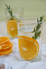 Two glasses of cool refreshing drink with orange and rosemary on a white napkin