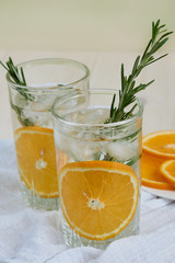 Two glasses of cool refreshing drink with ice, orange and rosemary on a white napkin