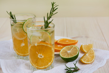 Two glasses of cool refreshing drink with ice, orange and rosemary on a white napkin