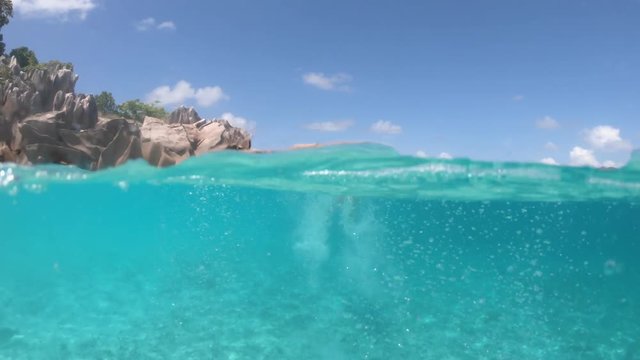 Split view of girl in apnea under and above the sea. Snorkeling dress woman at St. Pierre of Praslin satellite island, Seychelles. Travel lifestyle watersport activity. Fish and sealife in POV.