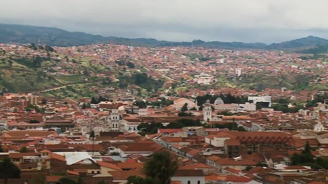 Handheld, panning, high, exterior, wide shot of the Sucre, Bolivia. Homes on flat terrain and rolling grassy hills.