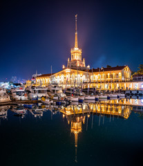 Marine Station of Sochi, illuminated with lights at night with reflection in water. Yachts and boats at the pier.