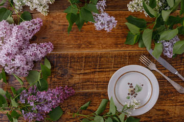 Plate and decor of flowers on the background of vintage wooden planks.Vintage background with lilac flowers and place under the text. View from above. Flat lay. Cutlery.