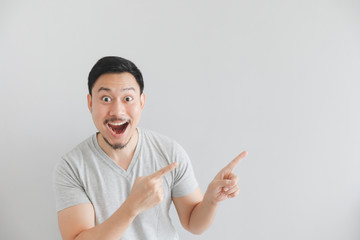 Wow and surprised face of man in grey t-shirt with hand point on empty space.