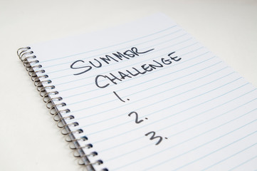 A spiral lined notebook with "Summer Challenge" and 1.2.3 written on it on a white background