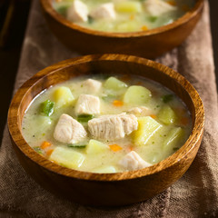Chicken and potato chowder soup with green bell pepper and carrot in wooden bowls, photographed on dark wood with natural light (Selective Focus, Focus in the middle of the soup)