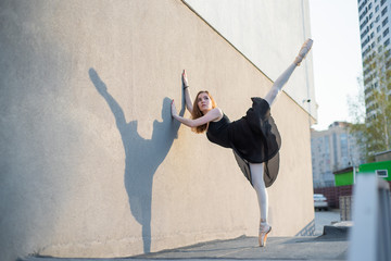 Ballerina in tutu posing standing near the wall. Beautiful young woman in black dress and pointe...