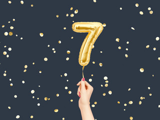Seven year birthday. Female hand holding Number 7 foil balloon. Seven-year anniversary background....