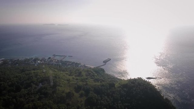 Aerial shot of small island with a small village and a jetty, surrounded by blue ocean in the afternoon. Shot at Marore Island, North Sulawesi, Indonesia.
