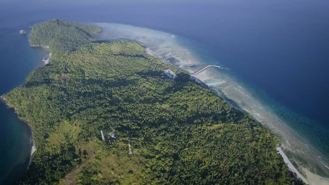 Aerial shot of small island with a small village and a jetty, surrounded by blue ocean in the afternoon. Shot at Marore Island, North Sulawesi, Indonesia.