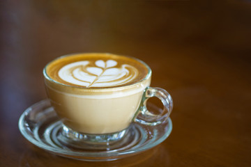Close-up of coffee hot cup with heart shaped latte art foam on wooden table. Beautiful art on a coffee mug. Space for text