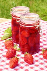 Strawberry jam in glass jars set and fresh strawberries on a wooden table with a red checkered napkin on a green vegetable background.Homemade jam. Canned berries. Healthy vegetarian 