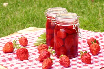 Strawberry jam in glass jars set and fresh strawberries on a wooden table with a red checkered napkin on a green vegetable background.Homemade jam.Summer berry jam. Canned berries. Healthy vegetarian 