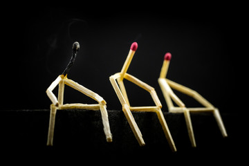 three characters made of matchsticks sad and sitting in the dark, one away from the other. One of them is depressed, weak and fading. Concept of solitude or social isolation, fatigue and exhaustion.