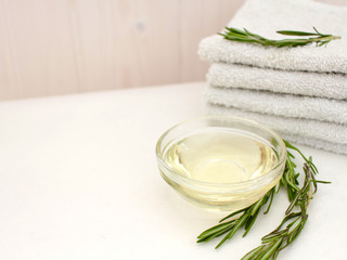 Rosemary oil and a branch of fresh rosemary with a stack of towels for face and body care on a wooden wall background. text entry area