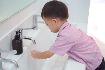Cute little Asian 2 - 3 years old toddler boy child washing hands by himself on sink and water drop from faucet in public toilet / bathroom for kids, Clean school washrooms - soft & selective focus