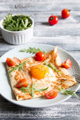 Crepes with eggs, cheese, arugula leaves and tomatoes. Galette complete. Traditional dish galette sarrasin.