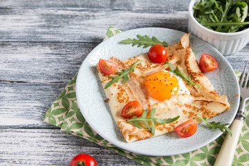 Fototapeta na wymiar Crepes with eggs, cheese, arugula leaves and tomatoes. Galette complete. Traditional dish galette sarrasin.