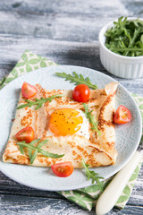Crepes with eggs, cheese, arugula leaves and tomatoes. Galette complete. Traditional dish galette sarrasin.