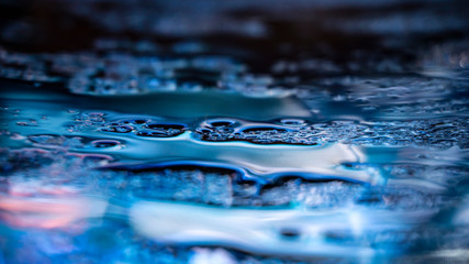 Dark background. Spilled liquid on the mirror surface, the reflection of neon lights, glare,...