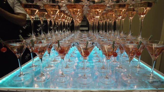 Many glasses for Martini with alcohol are on table in bar. Action. Mountains of wine glasses Martini with alcoholic drinks and cherries prepared for event barmen show