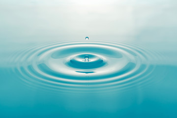 One blue drop of water on surface of water background
