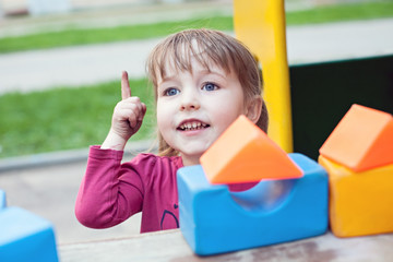 Fototapeta na wymiar funny white child girl with children bricks on outdoor playground background