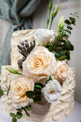 Two-tiered wedding cake beige. Decorated with handmade chocolate roses and artificial flowers. Photos in the interior. Hard light. Close-up.
