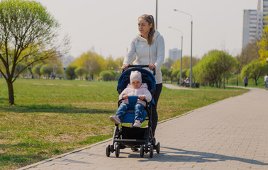 Fototapeta na wymiar Young mother with a baby in a stroller in a summer park.