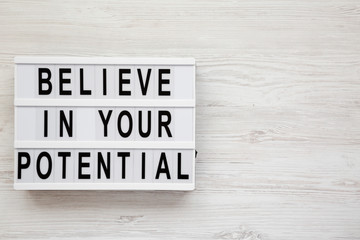 'Believe in your potential' words on a lightbox on a white wooden surface, top view. Flat lay, overhead, from above. Copy space.