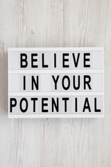 'Believe in your potential' words on a modern board on a white wooden background, top view. Flat lay, overhead, from above. Close-up.