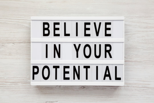 'Believe in your potential' words on a light box on a white wooden background, top view. Flat lay, overhead, from above.