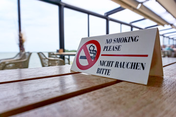 No smoking sign and text in English and German on a wooden table in a restaurant in the Netherlands 