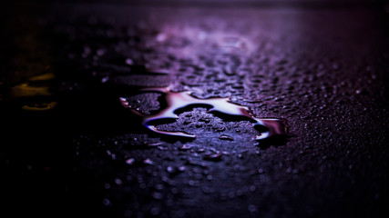 Dark background. Spilled liquid on the mirror surface, the reflection of neon lights, glare, blurred bokeh background. Neon, night view of the streets of a big city.