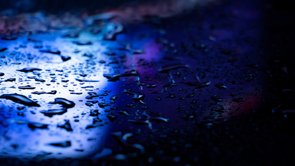 Dark background. Spilled liquid on the mirror surface, the reflection of neon lights, glare, blurred bokeh background. Neon, night view of the streets of a big city.