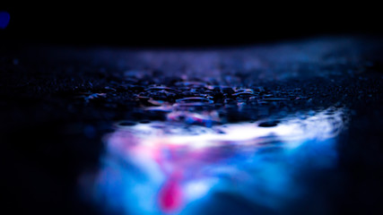 Dark background. Spilled liquid on the mirror surface, the reflection of neon lights, glare, blurred bokeh background. Neon, night view of the streets of a big city.