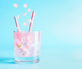 Summer beverage with rose petals and flowers. Refreshment drinks. Iced lemonade or cocktail on blue background
