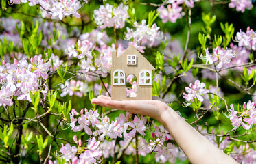      Girl holding a home symbol on a background of pink rhododendron 