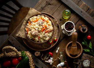 Overhead shot of yummy rice dish (plot, pilaf, curry) in wooden bowl stands on rustic table