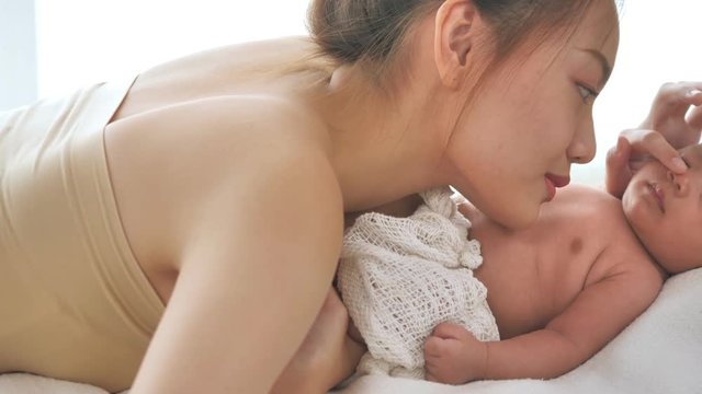 Bautiful young asian mother with her newborn baby lying on bed at home