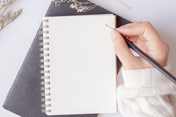 Top view young woman holding pencil with blank paper notebook on white table background.Dry flowers...