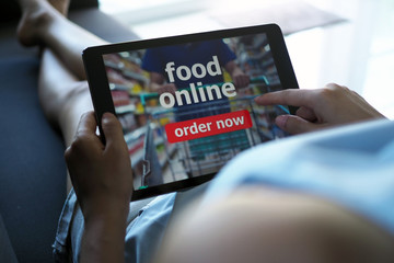 Women use tablets to order food online while lying on the couch at home.