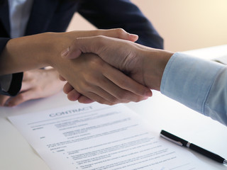 Two businessmen join hands to sign a contract after negotiating an investment and profit agreement.