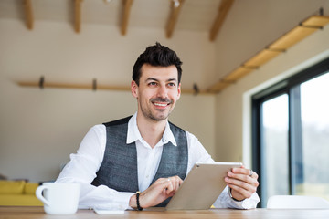 Young man with coffee sitting at the table, using tablet.